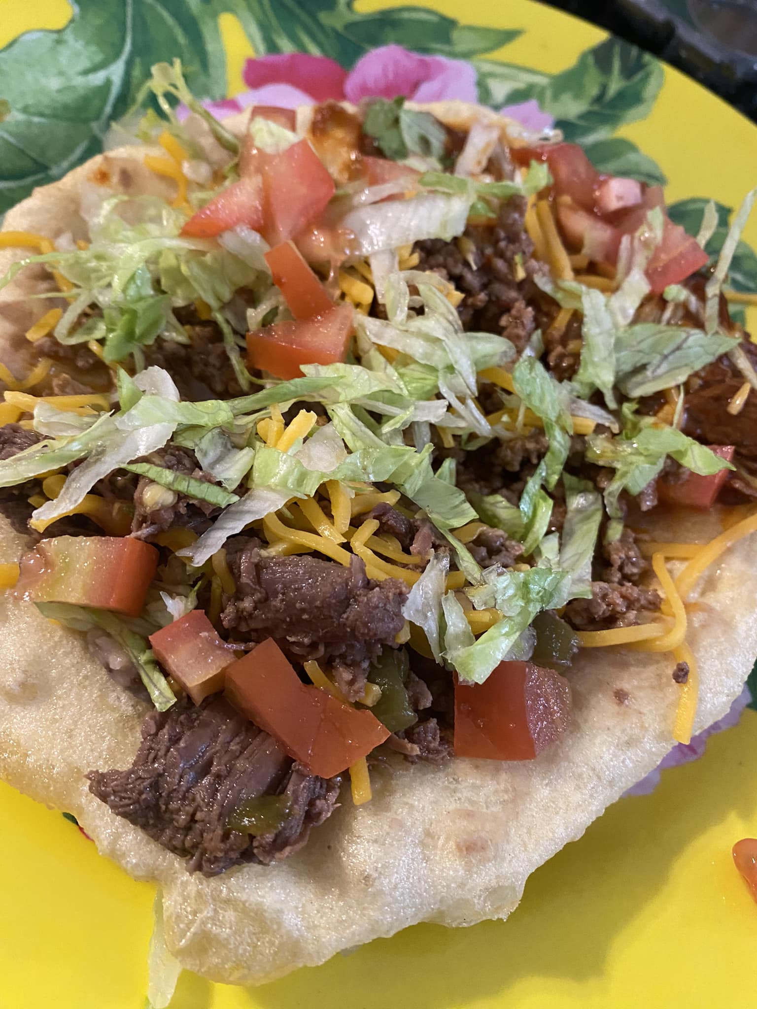 a photo of an "indian taco" which is frybread, meat, cheese, lettuce and tomatoes 